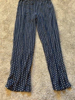 Mörkblå pyjamasbyxor med hjärtan - Mysiga mörkblå pyjamasbyxor från Lindex med vita hjärtan över hela tyget. Byxorna har resår i midjan och är gjorda i mjukt, stretchigt material som passar perfekt för chillkvällar hemma.