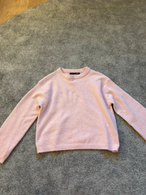 Ljusrosa stickad tröja 157 XS - Mysig ljusrosa stickad tröja från 157 med rund halsringning och ribbade muddar vid ärmslut och nederkant. Perfekt för lager på lager och enkel att matcha med jeans eller kjol. Klassisk och stilren modell.