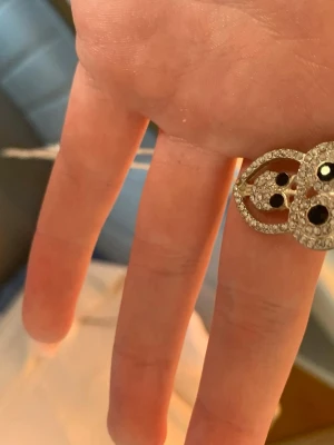 Statementring med svarta stenar - Unik statementring i guldtonad metall med glittrande vita och svarta stenar. Ringen har en bred, öppen design med flera detaljer och gnistrande stenar som fångar ljuset. Perfekt för dig som vill sticka ut med dina accessoarer.