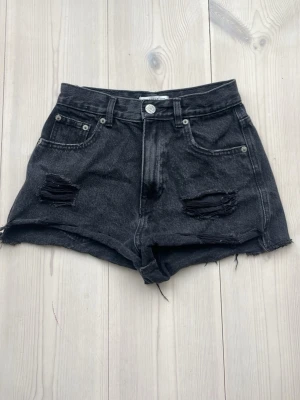 Svarta högmidjade jeansshorts - Säljer ett par svarta högmidjade jeansshorts med slitna detaljer och råa kanter. Perfekta för en somrig och trendig look❣️
