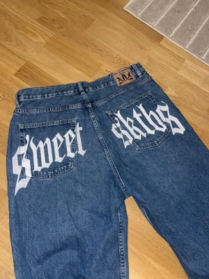 Blå baggy jeans Sweet Skthrs - Säljer ett par blå baggy jeans från Sweet Skthrs med cool vit text på bakfickorna. Jeansen har rak passform, klassisk femficksdesign och är gjorda i kraftigt denimtyg. Pris går att diskutera!💞