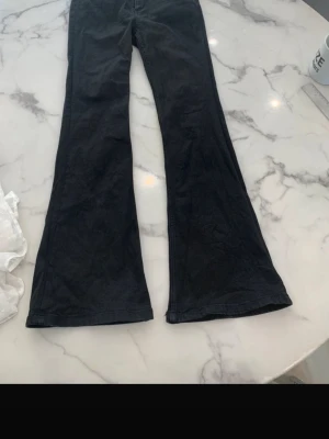 Svarta bootcut jeans - Säljer ett par svarta bootcut jeans med utsvängda ben. Jeansen har klassisk femficksdesign och är tillverkade i ett mjukt denimtyg. Perfekta för dig som gillar en retroinspirerad look och vill ha ett par jeans som sticker ut lite extra.