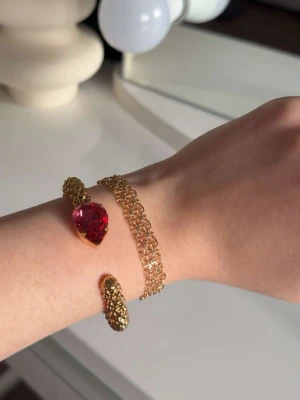 Guldarmband Caroline svedbom - Snyggt armband doppad i guld och en stor, droppformad rosa sten framtill. Armbandet är öppet och flexibelt, vilket gör det lätt att ta på och av. Perfekt för dig som vill ha något som sticker ut och känns lyxigt.