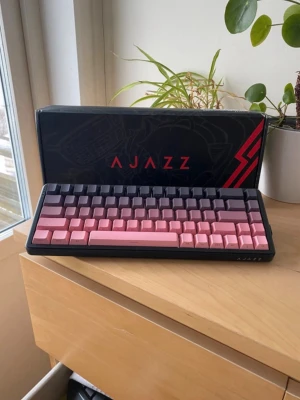 Ajazz mekaniskt tangentbord rosa/svart - Säljer ett Ajazz mekaniskt tangentbord med snygga rosa och svart tangenter. Kompakt design med svart ram, perfekt för gaming eller skrivbordet. Tangenterna är gjorda i plast och har en modern look. Levereras med originalkartong.