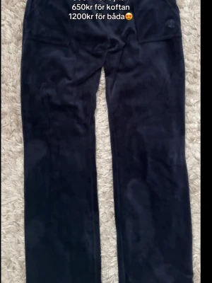 Marinblåa velourbyxor från Juicy Couture - Mörkblåa velourbyxor från Juicy Couture med raka ben och resår i midjan. Byxorna har två fickor med knappar bak och en diskret logga framtill. Perfekta för en chill och trendig look, kommer ej till användning! Tröjan är i M och byxan S!