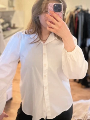 Vit skjorta med puffärm och knappar - Säljer en vit skjorta med klassisk krage och knappar framtill. Skjortan har långa puffärmar med resår vid ärmslut och en normal passform. Perfekt för dig som gillar stilrena plagg med en twist.