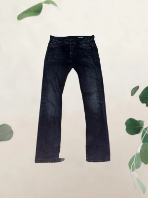 Replay jeans med fett tvät - Säljer ett par mörkblå jeans från Replay med klassisk femficksdesign med slitningar vid bensluten. Jeansen är tillverkade i ett mjukt denimtyg med lätt tvättad look. Perfekta för en avslappnad och trendig stil. Modell: Mijag. Storlek 30/34.