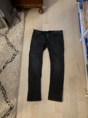 Svarta slim fit jeans från replay - Säljer ett par svarta slim fit jeans från replay med klassisk femficksdesign och raka ben. Jeansen har diskreta slitningar och är tillverkade i stretchig denim för skön passform. Perfekta till en avslappnad streetstyle-look.