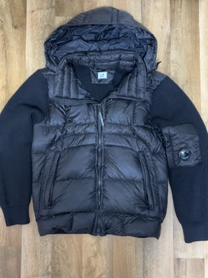 C.P COMPANY CARDIGAN - C.P. Company Cardigan – helt ny och oanvänd. Riktigt snygg hybridmodell med dunväst framtill och stickade ärmar för perfekt kombination av värme och stil. Modellen har C.P.-signaturen på ärmen och hög komfort.  Skick: 10/10 (ny) Storlek: m (passar även slim L)  Perfekt för dig som vill ha en mångsidig och modern cardigan i toppklass. Skriv vid intresse eller om du vill ha fler bilder.