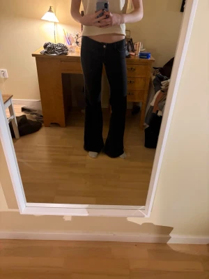 Svarta bootcut jeans med låg midja - Säljer ett par svarta bootcut jeans med låg midja och klassisk femficksmodell. Jeansen har utsvängda ben och stängs med knapp och dragkedja framtill. Perfekta för dig som gillar en retroinspirerad look.