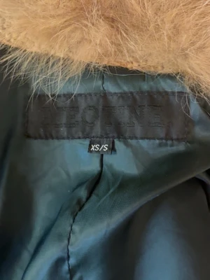 Beige kappa med pälskrage från Meotine - Säljer en beige kappa från Meotine med avtagbar päls. Xs/S. nypris ca 4,150kr. Saknas en knapp högst upp men ingen man brukar knäppa ändå. (märkte att jag hade tappat knappen nu när jag fotade den😅) nopprig men går att andvända nopper maskin. säljer därav billigt