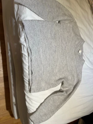 Ljusgrå stickad tröja - En enkel och stilren ljusgrå stickad tröja med rund halsringning och långa ärmar. Tröjan har ribbstickade muddar vid ärmslut och nederkant. Perfekt för lager-på-lager under kalla dagar.