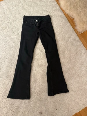 Svarta bootcut jeans - Säljer ett par svarta bootcut jeans med klassisk femficksmodell och utsvängda ben. Jeansen har normal midja och stängs med dragkedja och knapp. Perfekta för dig som gillar en retroinspirerad look och vill ha ett par bekväma jeans i stretchigt material.