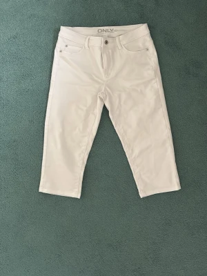 Vita jeans från ONLY, raka ben - Säljer ett par vita capri- jeans från ONLY med klassisk femficksmodell och raka ben. Jeansen har normal midja och stängs med knapp och dragkedja. Perfekta för en fräsch och stilren look.
