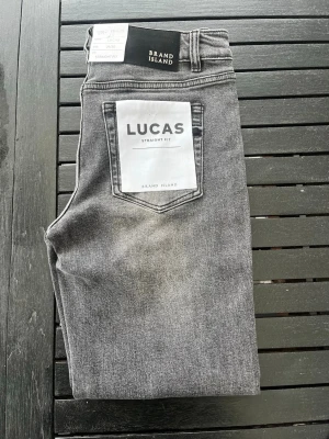 Gråa straight fit jeans Brand Island - Snygga gråa jeans från Brand Island i modellen Lucas Straight Fit. Jeansen har klassisk femficksdesign, normal midja och raka ben. Materialet är mjukt denim med en tvättad look som ger en avslappnad vibe. Jeansen är helt nya storlek W29 L32