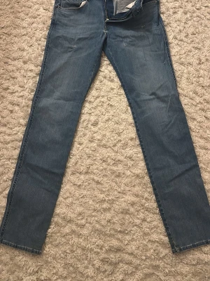 Blå slim jeans från Replay - Säljer ett par klassiska blå jeans från Replay med raka ben och normal midja. Jeansen har fem fickor, ljus tvätt och kontrastsömmar. Materialet är mjukt denim och bakfickorna har diskreta broderier. Perfekta för en avslappnad stil.