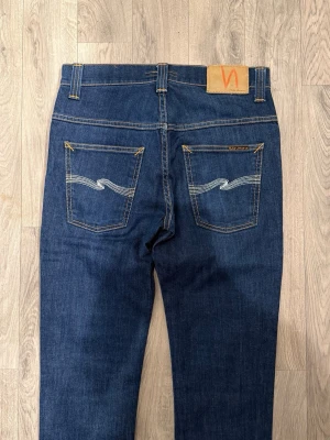 Nudie Jeans Thin Finn Dry Mörkblå W30/L32 - Slim Fit - Mycket fint skick. Mått - Midja: 37,5cm, Ytterbenslängd: 100cm, Benöppning: 16cm. Modellen är 185cm & 63kg. Hör av dig vid funderingar!🤝