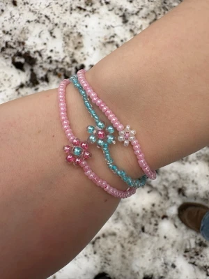 Söta pärlarmband med blommor - Tre handgjorda armband med små pärlor i rosa, blått och vitt. Varje armband har en söt blomdetalj av pärlor i matchande färger. Perfekta för att ge din outfit en gullig och färgglad touch. Elastiska och lätta att ta på.