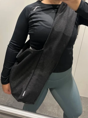 Svart axelväska i syntetmaterial - Säljer en svart jeans axelväska i stilren design. Väskan har en unik, mjuk form med bred axelrem och är tillverkad i syntetmaterial. Perfekt för dig som vill ha en enkel men trendig accessoar till vardagslooken.