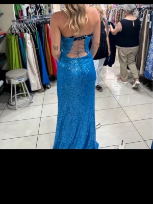 Blå glittrig långklänning med snörning - Säljer en blå långklänning med glittrigt tyg och snygg snörning i ryggen. Klänningen har en figurnära passform och är ärmlös, perfekt för dig som vill sticka ut. Materialet känns lyxigt och skimrar i ljuset. Går att tajta och lösa , funkar på Xs,S och M , Nypris 3200kr
