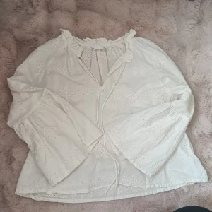 Vit broderad blus  - Söt vit blus med broderade detaljer och vida ärmar. Tillverkad i ett lätt och luftigt bomullstyg med romantiskt mönster.                         Katt finns i hemmet.                            