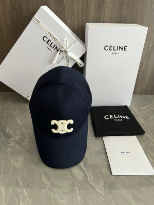 Mörkblå keps från Celine - Snygg mörkblå keps från Celine med broderad vit logga framtill. Klassisk böjd skärm och justerbar passform. Tillverkad i ett slitstarkt tyg som ger en exklusiv känsla. Perfekt accessoar för att lyfta din streetstyle.