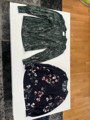 Två långärmade blusar med mönster - Säljer två snygga blusar: en grön med abstrakt mönster och en mörkblå med blommigt tryck i rosa och beige toner. Båda har rund halsringning och långa ärmar. Perfekta att matcha med jeans eller kjol för en trendig look.
