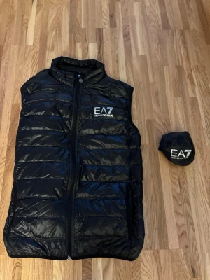 Svart väst - EA7 Emporio Armani - Snygg svart väst från EA7 Emporio Armani med quiltad design och dragkedja framtill. Västen har logga på bröstet. Kommer med tillhörande förvaringspåse