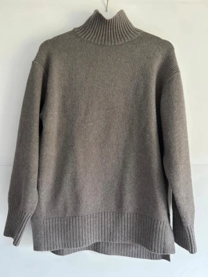 Grå-beige stickad tröja med polokrage och slits  - Mysig grå stickad polotröja med hög krage och slits i sidorna. Något nopprig. Djur och rökfritt hem.