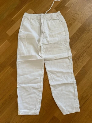 Vita linnebyxor från H&M - Säljer ett par vita linnebyxor från H&M med avslappnad passform och resår i midjan samt dragsko. Byxorna har raka ben och är tillverkade i ett luftigt linnematerial, perfekta för en chill och stilren look.