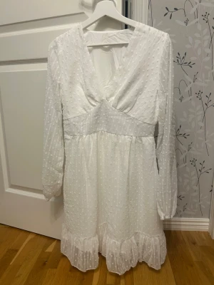 Zara Vit kort omlottklänning med volang i storlek m - Superfin vit kortklänning med omlottliv, v-ringning och volangkant nertill. Klänningen har långärmade ärmar och ett diskret prickigt mönster i tyget. Perfekt för sommarens alla tillfällen!Storlek M och fin skick använd en gång på studenten. 