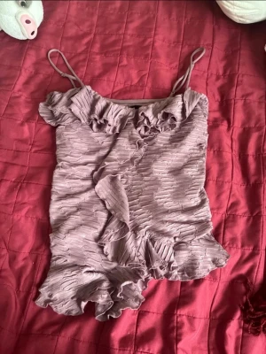 Ljuslila volangtop från BikBok - Supersöt ljuslila linnetopp från BikBok med volangdetaljer och smala axelband. Toppen har en plisserad struktur och är perfekt för dig som gillar feminina detaljer och en trendig look.