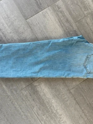 Acne Toj U - jeans med hög midja - Säljer ett par ljusblå mom jeans i klassisk denim med hög midja och raka ben. Jeansen har fem fickor, bälteshällor och en liten slitning på vänster lår och har en avslappnad passform.