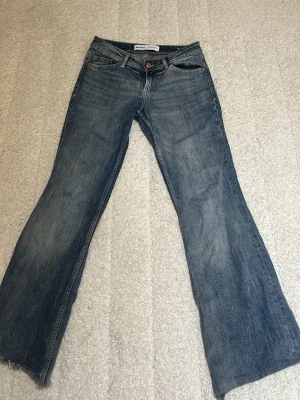 Blå bootcut jeans från bershka - Ett par klassiska blå bootcut jeans från Crocker med fem fickor och låg midja. Jeansen har en lätt tvättad look och vida ben som ger en retrovibe. Perfekta för dig som gillar en avslappnad och trendig stil.