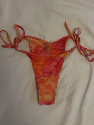 Blommig bikiniunderdel med knyt - Säljer en snygg bikiniunderdel från SHEIN i blommigt mönster med rosa och orange toner. Triangle bikini i storlek M !! TVÄTTAS INNAN !!