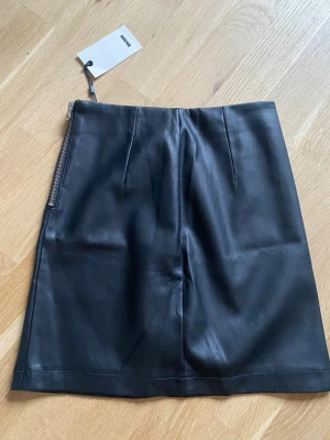 Svart skinnkjol NY - Säljer en svart skinnkjol/minikjol från Bikbok, dragkedja i sidan. Helt ny och oanvänd med prislapp kvar!