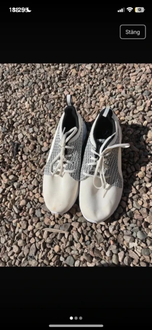 Vita och grå sneakers med mesh - Snygga sneakers i vitt och grått med ovandel i meshmaterial och klassisk snörning. Skorna har en låg profil och svart detalj på hälen. Perfekta för en sportig och stilren look. jättefina men det finns en fläck på foten. Har ej provat och tagit bort den