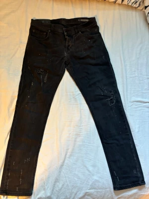 Svarta dundup jeans med slitningar (george) - Säljer ett par svarta jeans från dundup modell george med coola slitningar och distressed detaljer på benen. Jeansen har klassisk femficksdesign och är i stretchigt material för en bekväm passform. 