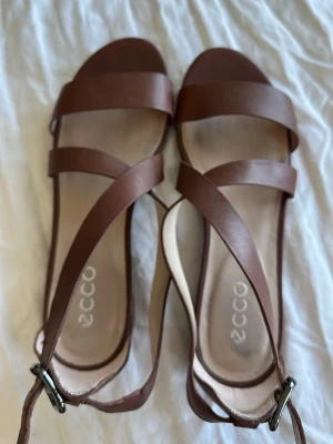 Bruna ECCO sandaler i läder - Snygga bruna sandaler från ECCO med klassisk design. De har breda remmar i äkta läder och justerbart spänne vid ankeln. Perfekta för sommaren och passar till många olika outfits.