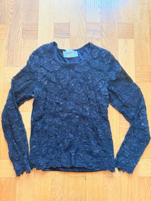 Svart spetsblus med lång ärm - Supersnygg svart blus från Petite Sophisticate, köpt på marknad i Italien, med lång ärm och vackra spetsdetaljer över hela toppen. Blusen är fodrad undertill över kroppen men inte ärmarna. Perfekt festtopp!
