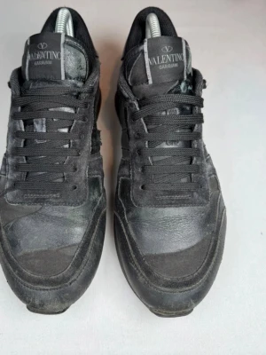 Svarta sneakers från Valentino Rockrunners - Snygga svarta sneakers från Valentino Garavani med klassisk låg siluett. Skorna har en mix av mocka och läderdetaljer, svarta skosnören och diskret logga på plösen. Perfekta för dig som gillar stilrena och exklusiva sneakers. Kan snacka pris