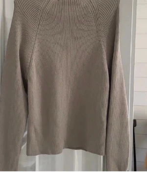 Beige ribbad topp från Zara - Säljer en grå ribbad topp från Zara med dekorativa knappar längs axlarna. Toppen har en croppad passform och är tillverkad i mjukt material som känns skönt mot huden. Perfekt att styla med jeans eller kjol.