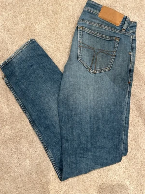 Sköna klassiska Tiger of sweden jeans i en ljusare blå ton - Snygga blå jeans som är  Perfekta till en avslappnad stil och tillverkade i bomull för skön känsla. Jeansen har en skada under men är lagade.