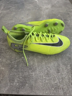 Nike gula fotbollsskor med dobbar - Snygga fotbollsskor från Nike i neon-gult med svarta och silverfärgade detaljer. Skorna har klassisk snörning och dobbar för bra grepp på planen. Tillverkade i syntetmaterial för lätt känsla och bra bollkontroll.