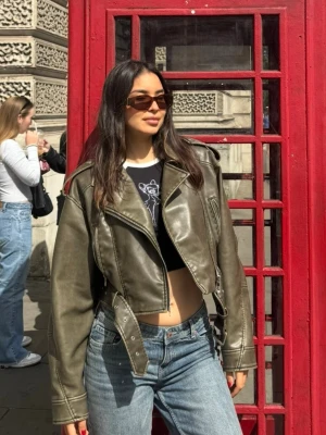 cropped skinnjacka Zara i M - Snygg olivgrön skinnjacka med croppad passform och breda slag. Jackan har dragkedja, bälte i midjan och coola detaljer som markerade sömmar. Perfekt för dig som vill ha en edgy stil och gillar streetmode. Från Zara i storlek M