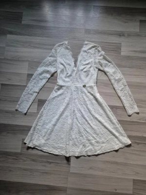Vit spetsklänning med v-ringning - Vit kortklänning från Chiara Forthi i spets med lång ärm och djup v-ringning. Klänningen har en markerad midja och lätt utställd kjol. Perfekt för dig som gillar romantisk och feminin stil.