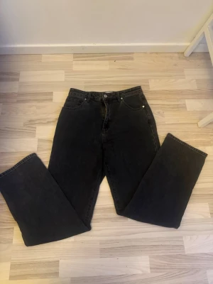 Svarta raka jeans med hög midja - Säljer ett par svarta jeans med rak passform och hög midja. Jeansen har klassisk femficksdesign och stängs med knapp och dragkedja. Perfekta för en avslappnad och trendig look. Materialet är denim i bomull.