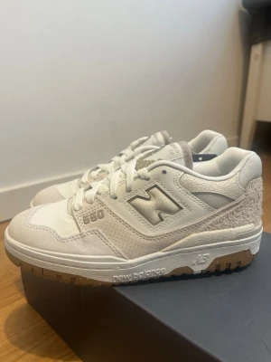 New Balance 550 beige/vita sneakers - Snygga New Balance 550 sneakers i vitt med beige detaljer. Sko storlek: 36. Skorna har en mix av läder och mocka samt en unik textur på hälen. Klassisk siluett med lågt skaft och gummisula. Perfekta för dig som gillar stilrena och trendiga sneakers. Väldigt bekväma att gå på promenader samt springa med, lätt att tvätta av. 