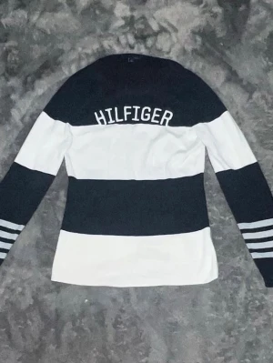 Tommy Hilfiger Randig Långärmad Tröja  -  riktigt fräsch marinblå och vitrandig tröja. Klassisk design med broderat "HILFIGER" över bröstet och snygga detaljer vid ärmsluten.  • Skick: 10/10  helt felfri  • Material: Mjuk och stretchig bomullskvalitet. 66cm lång och 60cm arm längd   