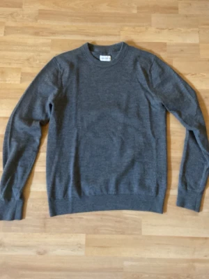 Grå stickad tröja These Glory Days - Snygg grå stickad tröja från These Glory Days med rund halsringning och klassisk passform. Tröjan är enkel och stilren, perfekt att matcha med jeans eller chinos. Materialet känns mjukt och bekvämt mot huden.